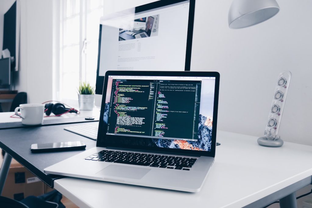 A laptop displaying coding on the screen, with a cup and headphones on a desk in a modern office setting.